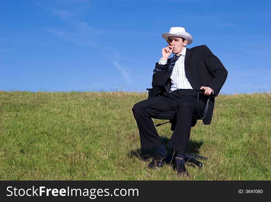 Young businessman sitting on a chair on the meadow :-). Young businessman sitting on a chair on the meadow :-)