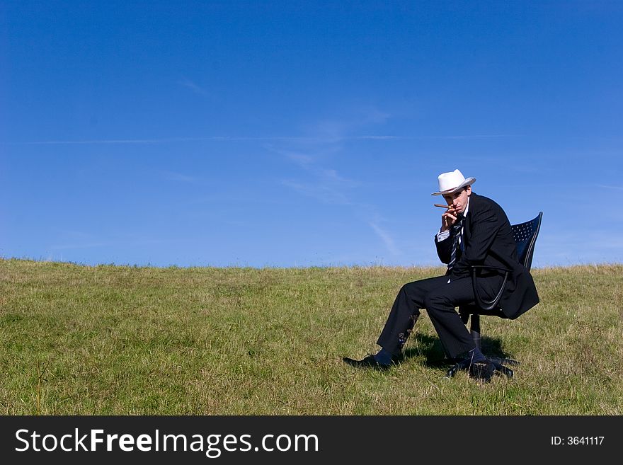 Young businessman sitting on a chair on the meadow :-). Young businessman sitting on a chair on the meadow :-)