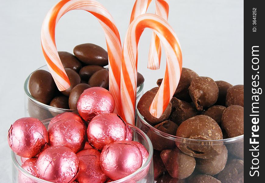 Chocolate covered almonds and peanuts, foil wrapped chocolate, and candy canes against a white background. Chocolate covered almonds and peanuts, foil wrapped chocolate, and candy canes against a white background.