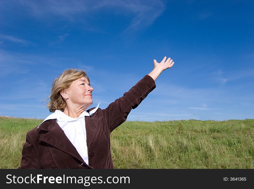 Mature and cheerful, joyful and happy woman enjoying life on a meadow, pointing at something/ showing something with her hand. Mature and cheerful, joyful and happy woman enjoying life on a meadow, pointing at something/ showing something with her hand.