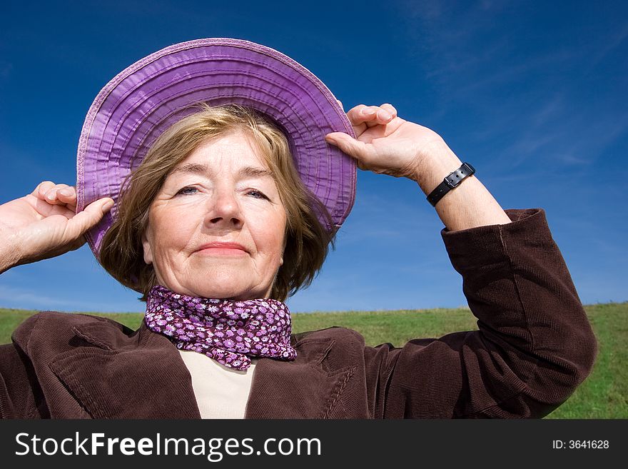 Mature and cheerful, joyful and happy woman enjoying life on a meadow, having fun with her violet hat - presenting good condition and healthy life :). Mature and cheerful, joyful and happy woman enjoying life on a meadow, having fun with her violet hat - presenting good condition and healthy life :)