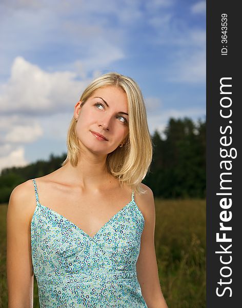 Beautiful blond girl in the field, blue cloudy sky behind her