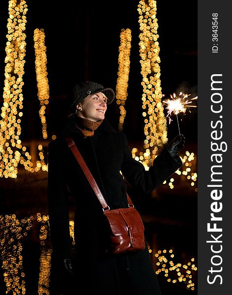 Beautiful happy girl with Christmas fireworks on abstract blurred background