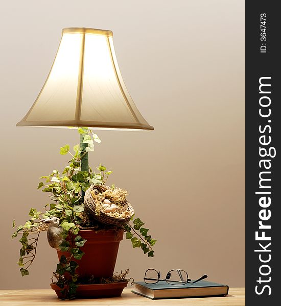 Closed book with reading glasses by a lit table lamp. Closed book with reading glasses by a lit table lamp.