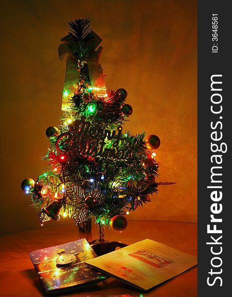 Small, but beautifully lit up and decorated artificIal Christmas tree with greeting cards at base.