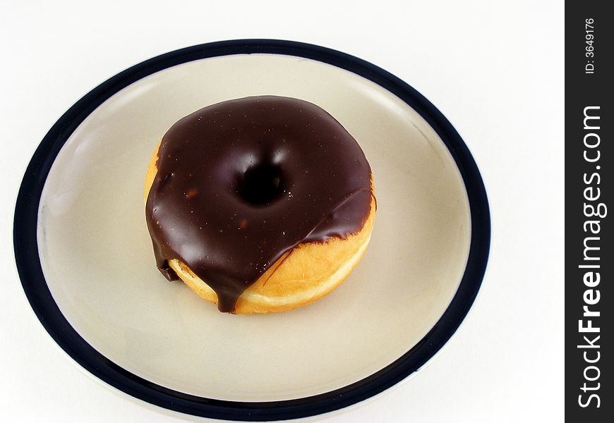 A chocolated iced donut on a plate against a white background. A chocolated iced donut on a plate against a white background.