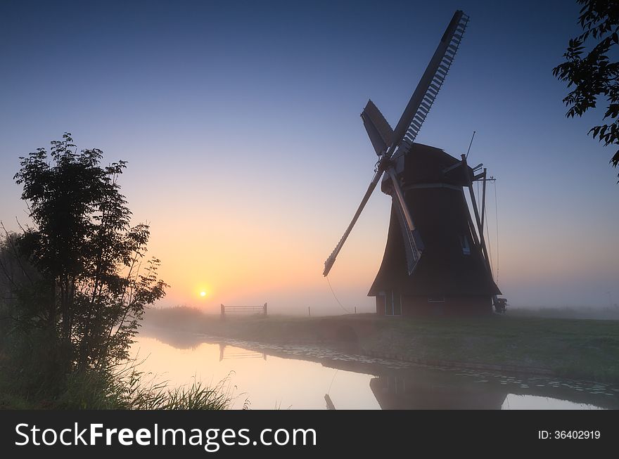 Traditional windmill during a foggy summer sunrise in the Dutch countryside. Traditional windmill during a foggy summer sunrise in the Dutch countryside.