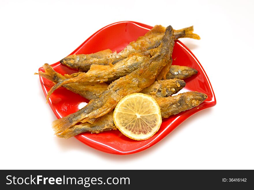 Fried fish and lemon on a red plate, isolated background. Fried fish and lemon on a red plate, isolated background