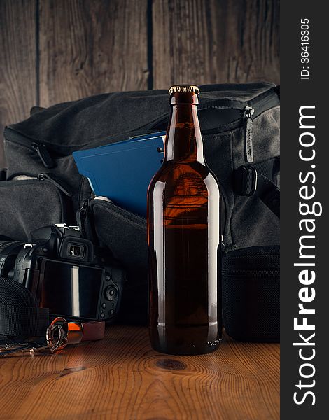 Bottle of beer in the background of several items. Photocamera, coach bag, notebook, keys, wooden table. Bottle of beer in the background of several items. Photocamera, coach bag, notebook, keys, wooden table.