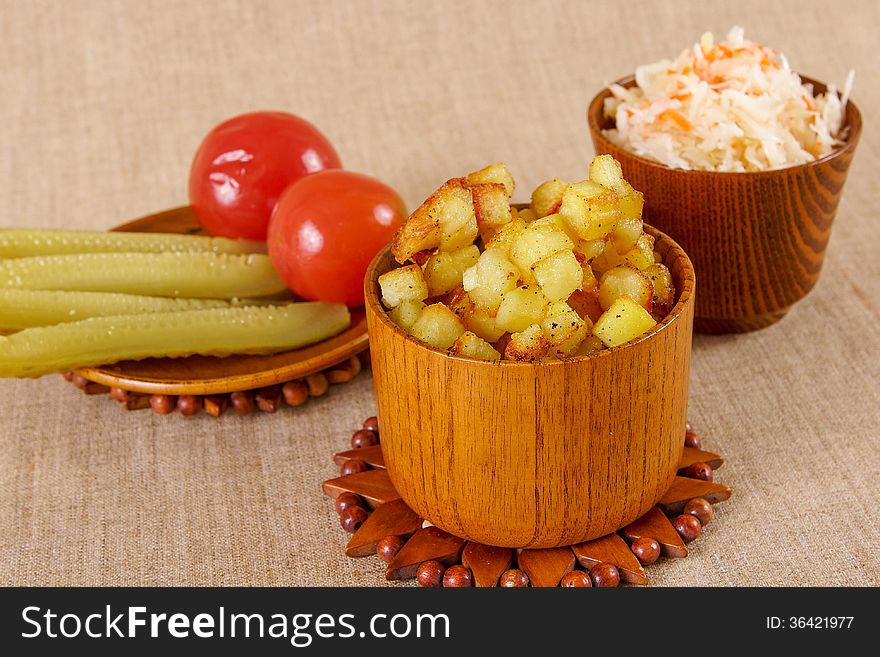 Fried potato cubes with sour cabbage and pickle in a wooden bowl. Fried potato cubes with sour cabbage and pickle in a wooden bowl