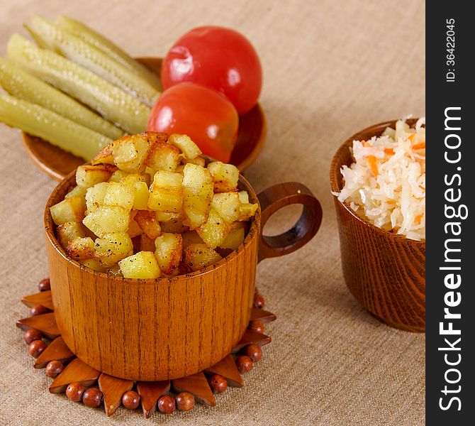 Fried potato cubes with sour cabbage and pickle in a wooden bowl. Fried potato cubes with sour cabbage and pickle in a wooden bowl