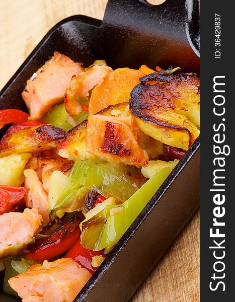 Homemade Salmon Stew with Potato, Red Bell Pepper, Leek and Carrot in Black Frying Pan closeup on Wooden background