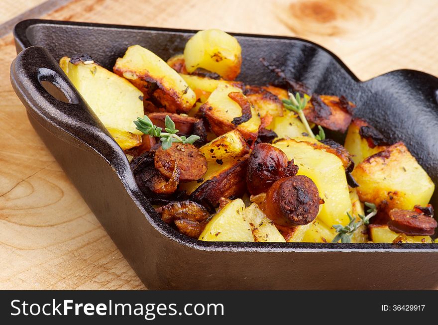 Tasty Homemade Roasted Sausages and Potato Stew in Black Frying Pan closeup on Wooden background