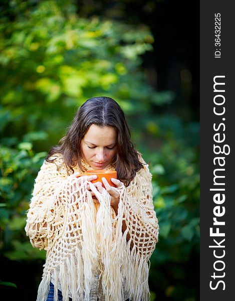 Young woman, wrapped in a knitted shawl, drinking tea in the forest. Young woman, wrapped in a knitted shawl, drinking tea in the forest