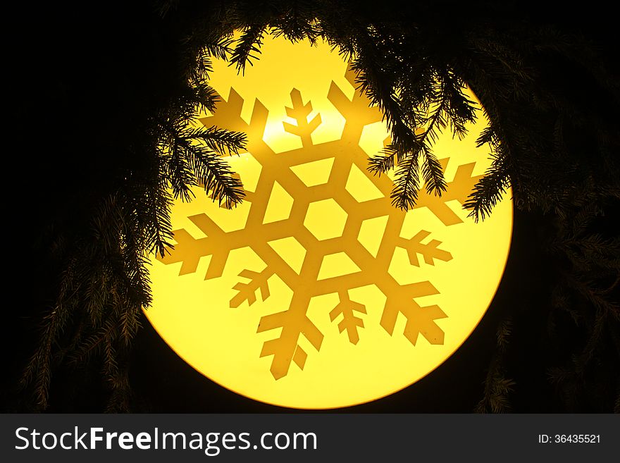 Symbol of a snowflake on yellow background lighted and between fir branches. Symbol of a snowflake on yellow background lighted and between fir branches.