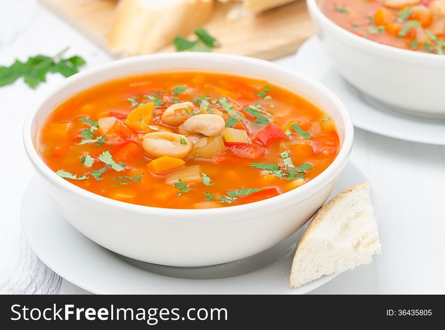 Vegetable soup with white beans in a bowl on a white table horizontal. Vegetable soup with white beans in a bowl on a white table horizontal