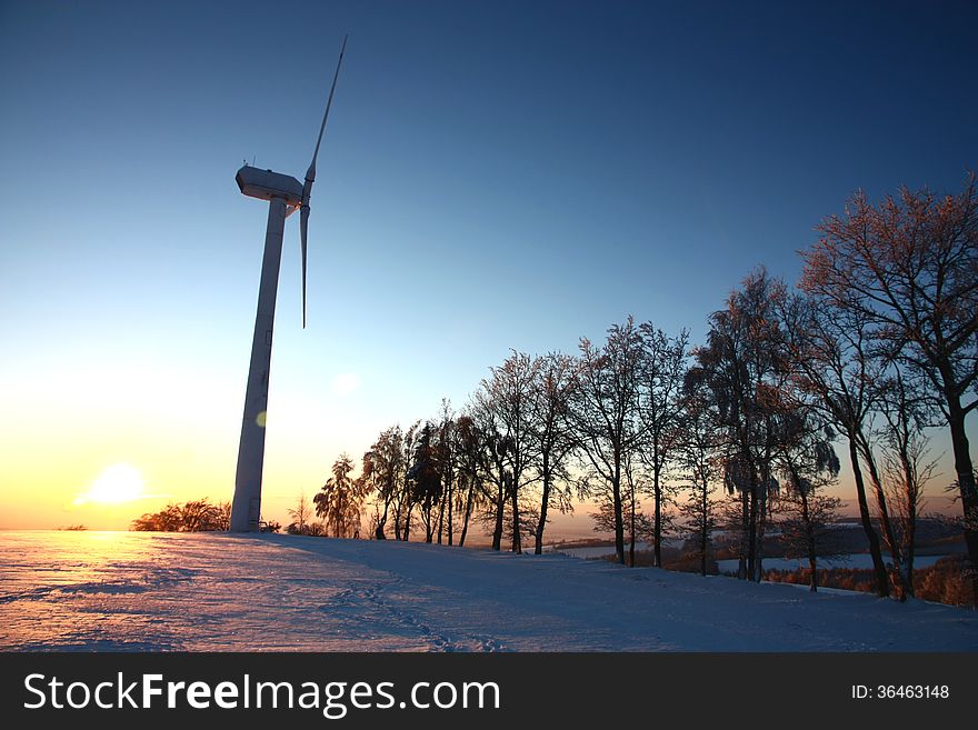 Mast wind turbine in a winter landscape, setting sun and wind power