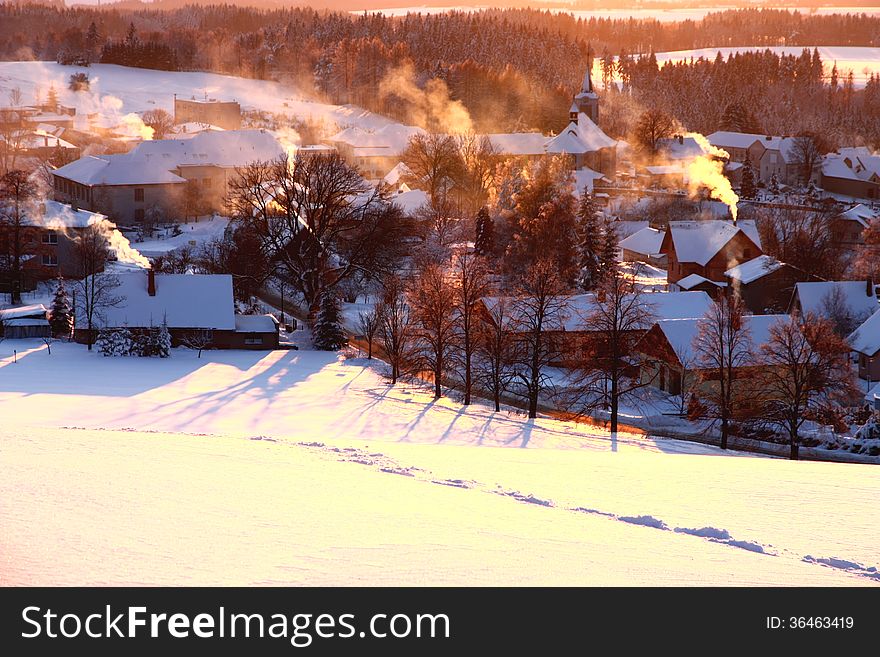 Village in winter at sunset, smoking chimneys in the village