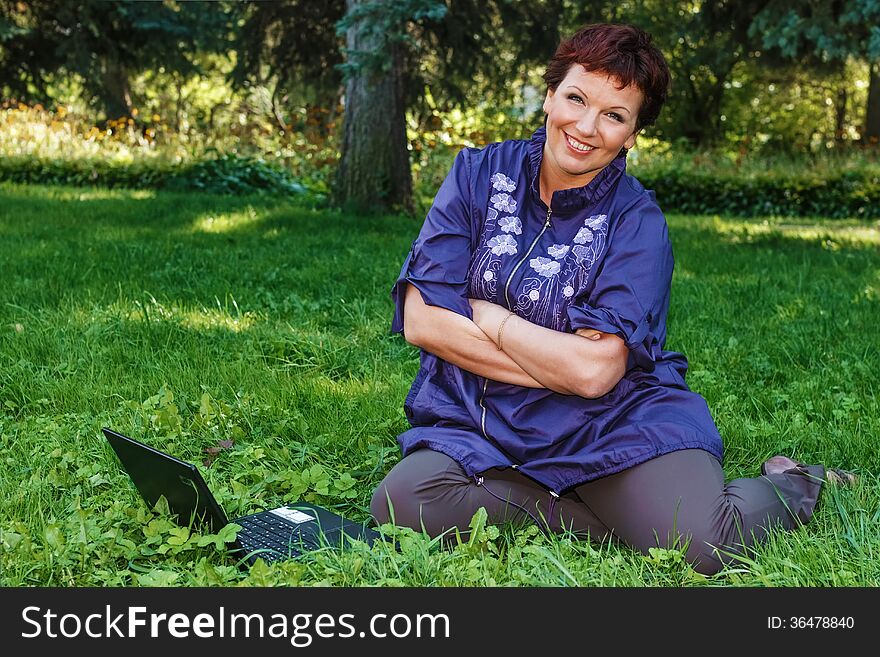 Beautiful woman sitting cross-legged with her laptop on her lap on a green lawn. Beautiful woman sitting cross-legged with her laptop on her lap on a green lawn.