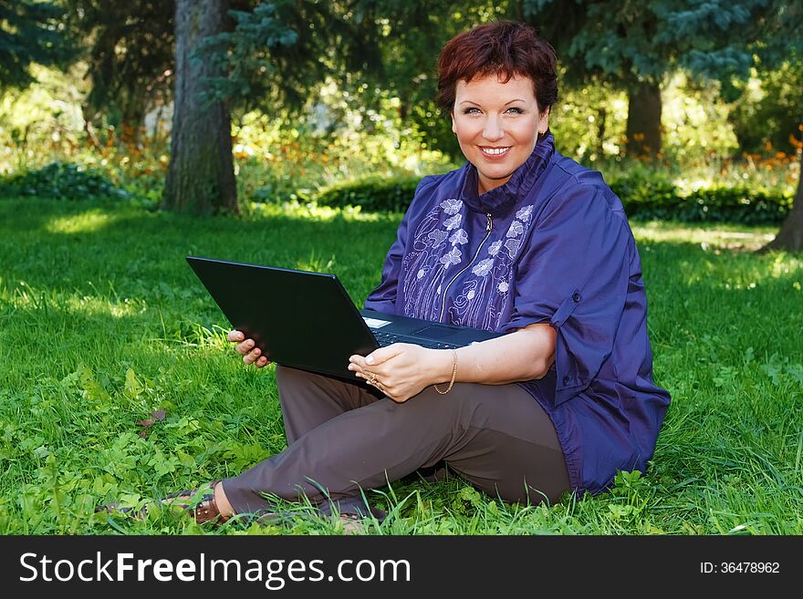 Woman with laptop on green lawn.