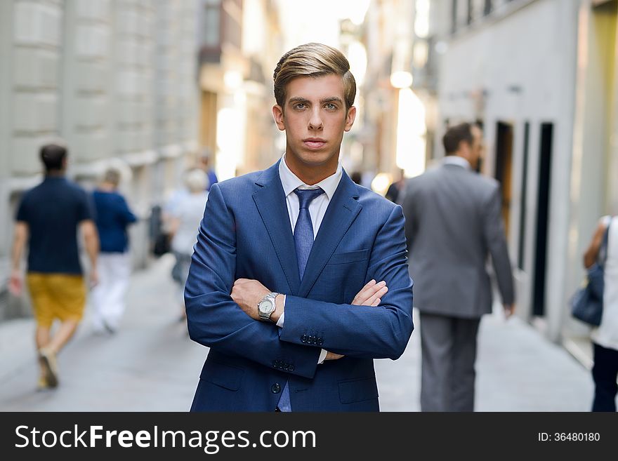 Portrait of an attractive young businessman in urban background wearing blue suit a necktie. Blonde hair