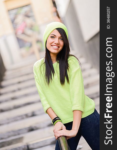 Portrait of brunette young woman with green eyes, wearing green casual clothes and hat, in urban background. Portrait of brunette young woman with green eyes, wearing green casual clothes and hat, in urban background