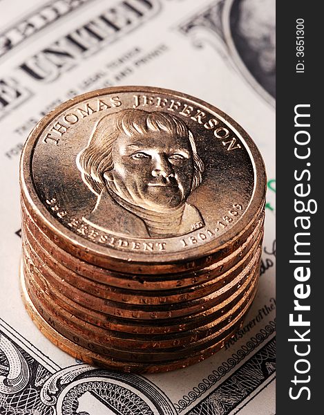 Vertical close-Up of a Jefferson dollar coin on a stack of dollar coins with an out-of-focus paper dollar bill in the background. Vertical close-Up of a Jefferson dollar coin on a stack of dollar coins with an out-of-focus paper dollar bill in the background.