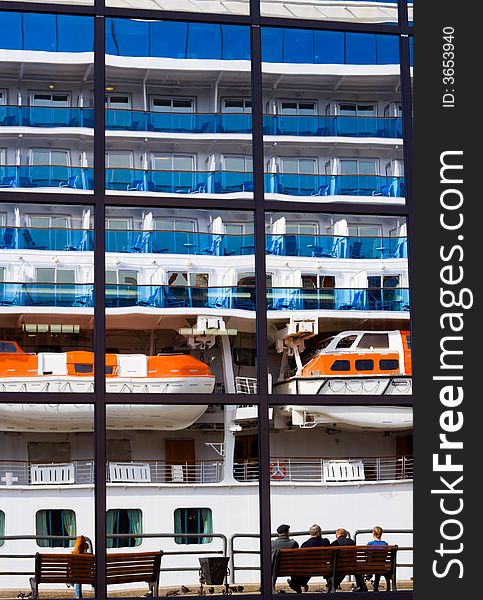 Russia. Round the world cruise ship is leaving from port Vladivostok. Reflection of the liner on the marine passenger terminal. Some people siting here on a benches. Russia. Round the world cruise ship is leaving from port Vladivostok. Reflection of the liner on the marine passenger terminal. Some people siting here on a benches.