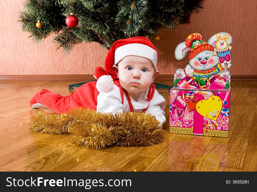 Little baby as Santa in red cap laying on the floor with gifts. Little baby as Santa in red cap laying on the floor with gifts