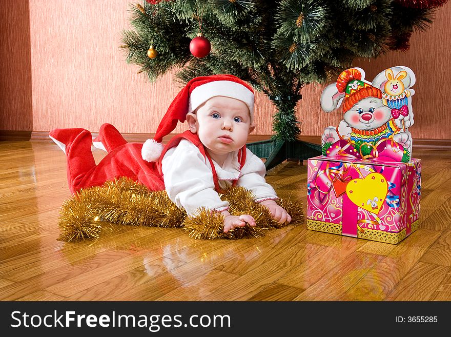 Little baby as Santa in red cap laying on the floor with gifts. Little baby as Santa in red cap laying on the floor with gifts