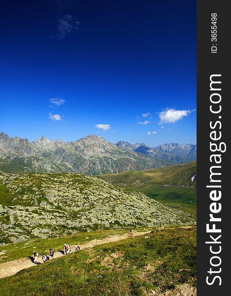 Trekkers walking on the trail by a summer afternoon with a superb panorama on mountains.