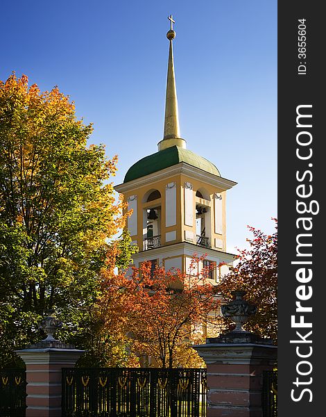 Autumn belltower on a background of the blue sky, surrounded by multi-coloured autumn trees. Autumn belltower on a background of the blue sky, surrounded by multi-coloured autumn trees