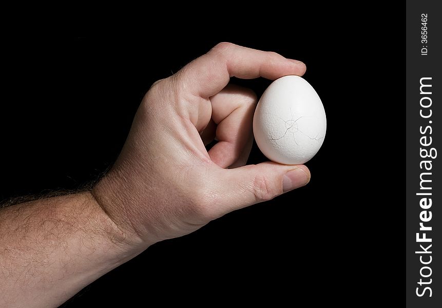 The hand holds an egg with cracks on a black background. The concept of destruction. The hand holds an egg with cracks on a black background. The concept of destruction.