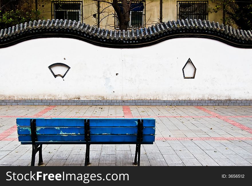 A blue bench sits in a small public garden in China, enclosed by a traditional Chinese wall. A blue bench sits in a small public garden in China, enclosed by a traditional Chinese wall.