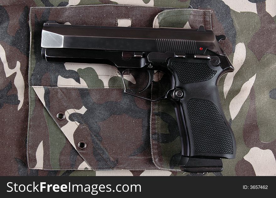 A 9mmP pistol on a camouflaged military style garment.  Photographed in a studio. A 9mmP pistol on a camouflaged military style garment.  Photographed in a studio.