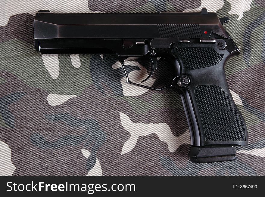 A 9mmP pistol on a camouflaged military style garment. Photographed in a studio. A 9mmP pistol on a camouflaged military style garment. Photographed in a studio.