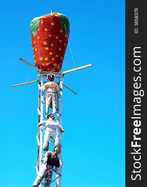 Three scarecrows hanging from a metal structure with a red strawberry on top of the structure. Three scarecrows hanging from a metal structure with a red strawberry on top of the structure