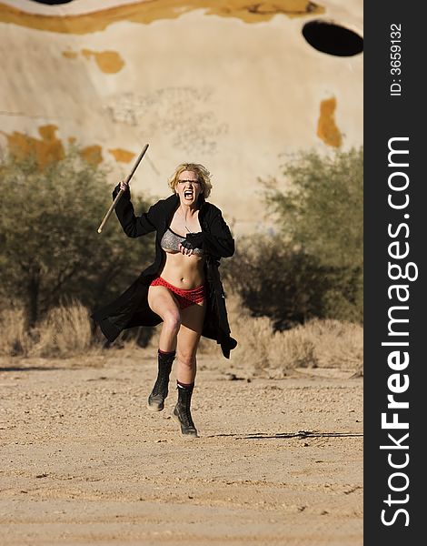 Female science fiction model in a desolate location attacking with a wooden stick. Female science fiction model in a desolate location attacking with a wooden stick.