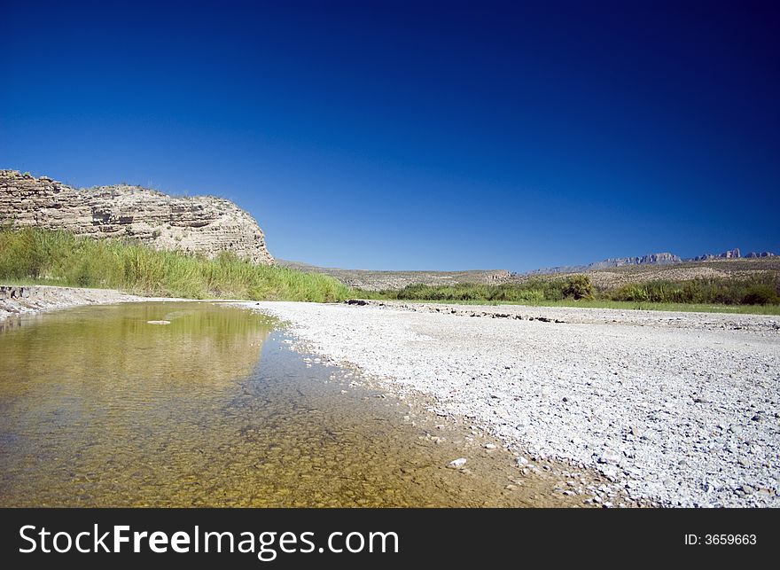 A distant cliff reflecting in the shallow waters of a riverbed. A distant cliff reflecting in the shallow waters of a riverbed.