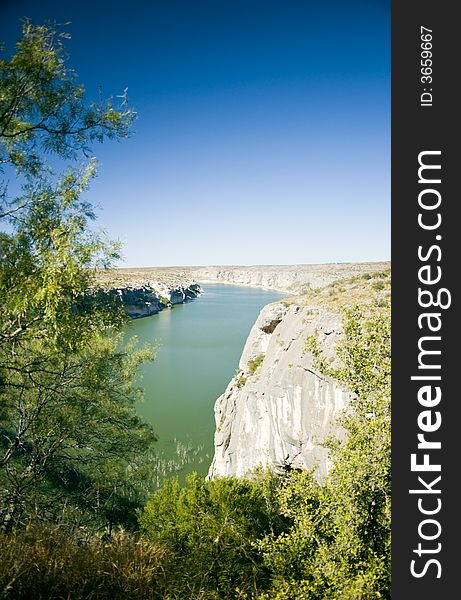 A wide green river bodered by rocky cliffs and enveloped in a bright blue cloudless sky. A wide green river bodered by rocky cliffs and enveloped in a bright blue cloudless sky.