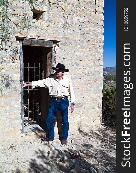 A man in western attire standing outside an old ruin of a jail. A man in western attire standing outside an old ruin of a jail