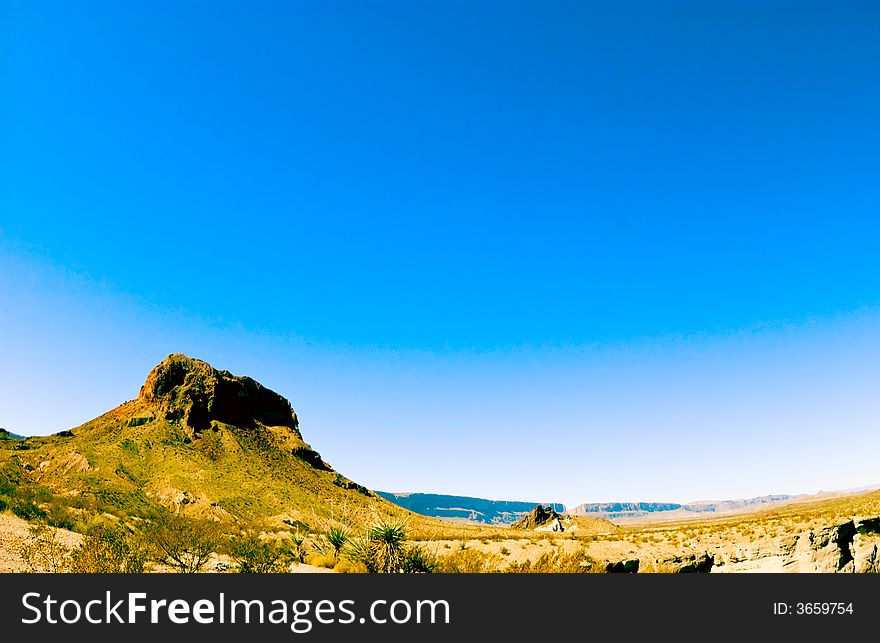 A rock formation reaching into a beautiful, bright, blue expanse of sky.