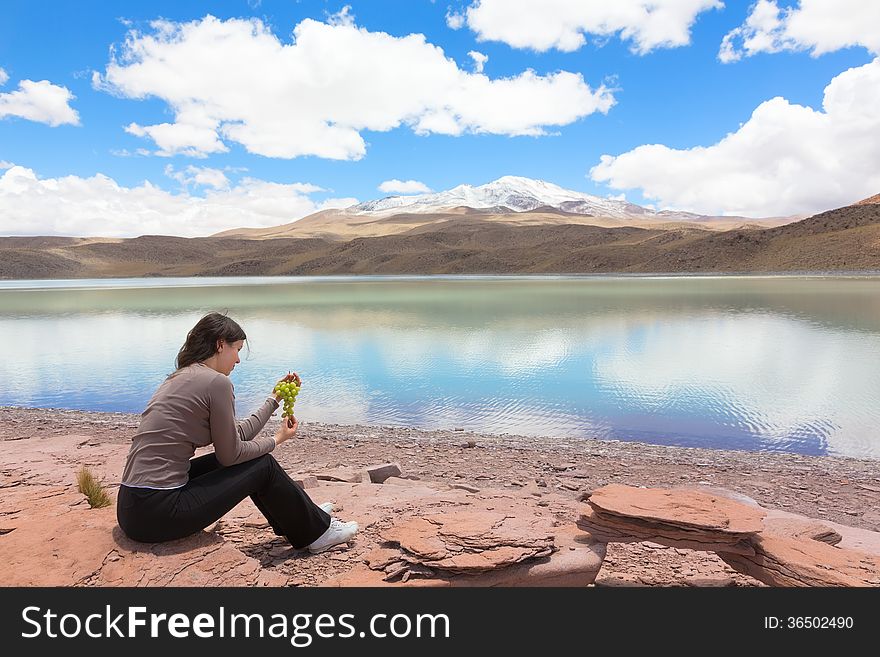 Woman sitting at the shore of lagoon Celeste, Bolivia and eating grape. Woman sitting at the shore of lagoon Celeste, Bolivia and eating grape