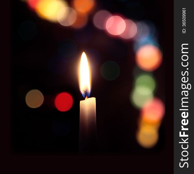 Flame of a candle on a dark background with colored bokeh