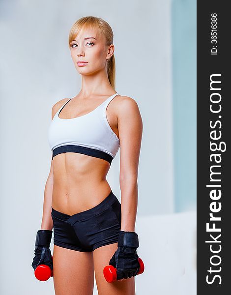 Blonde sporty woman holding red dumbbells