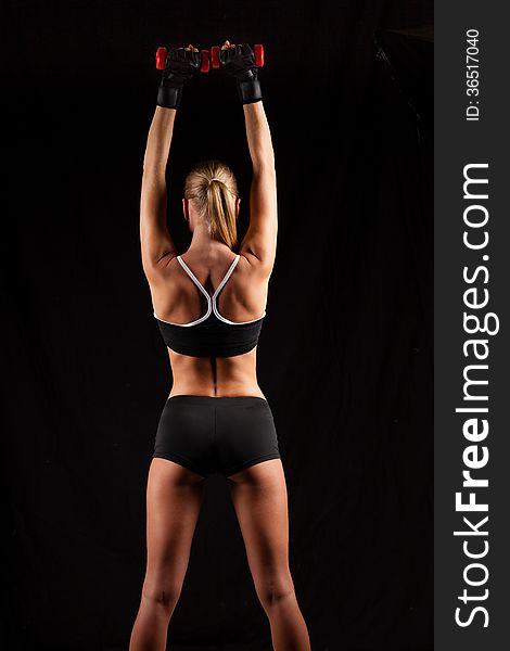 Blonde sporty woman holding red dumbbells in the dark