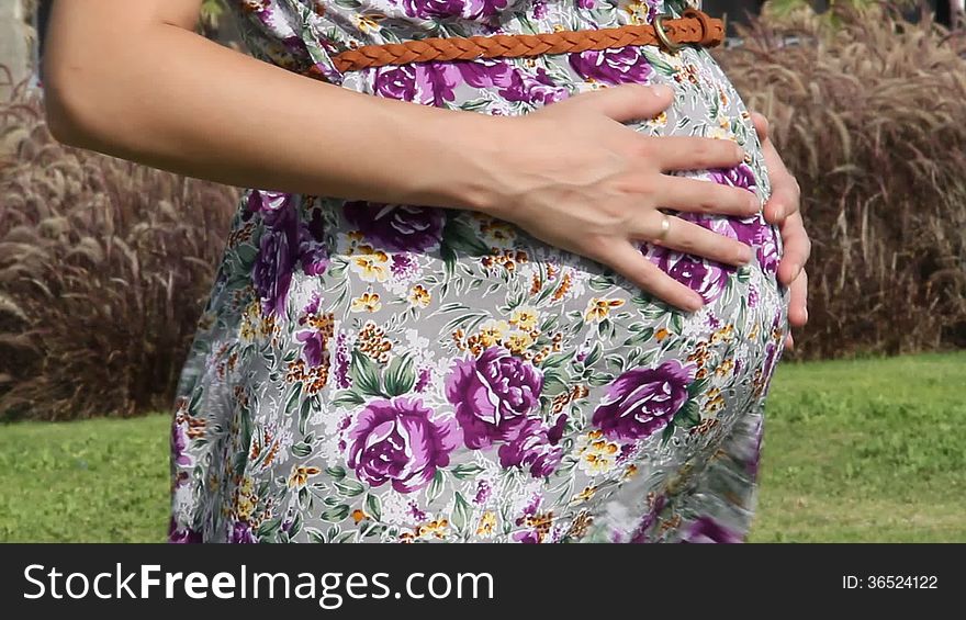 Happy Pregnant woman stroking her belly, outdoors