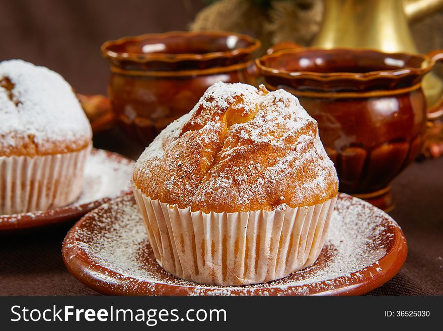 Fresh muffins on a brown table with a cups of coffee and coffee pot