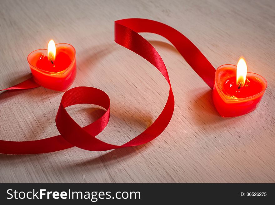 Two burning heart shaped candles with red ribbon. Two burning heart shaped candles with red ribbon.