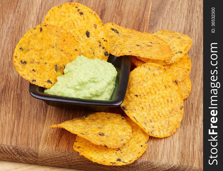 Arrangement of Tortilla Chips and Guacamole Sauce in Black Bowl closeup on Wooden Board